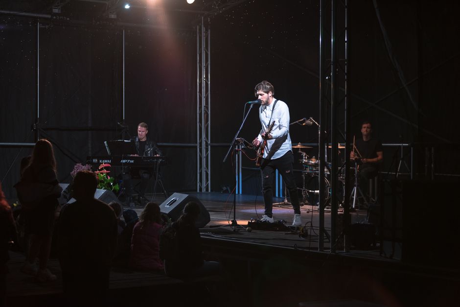 Dynamic band performing live with guitar, keyboard, and drums on an illuminated stage.