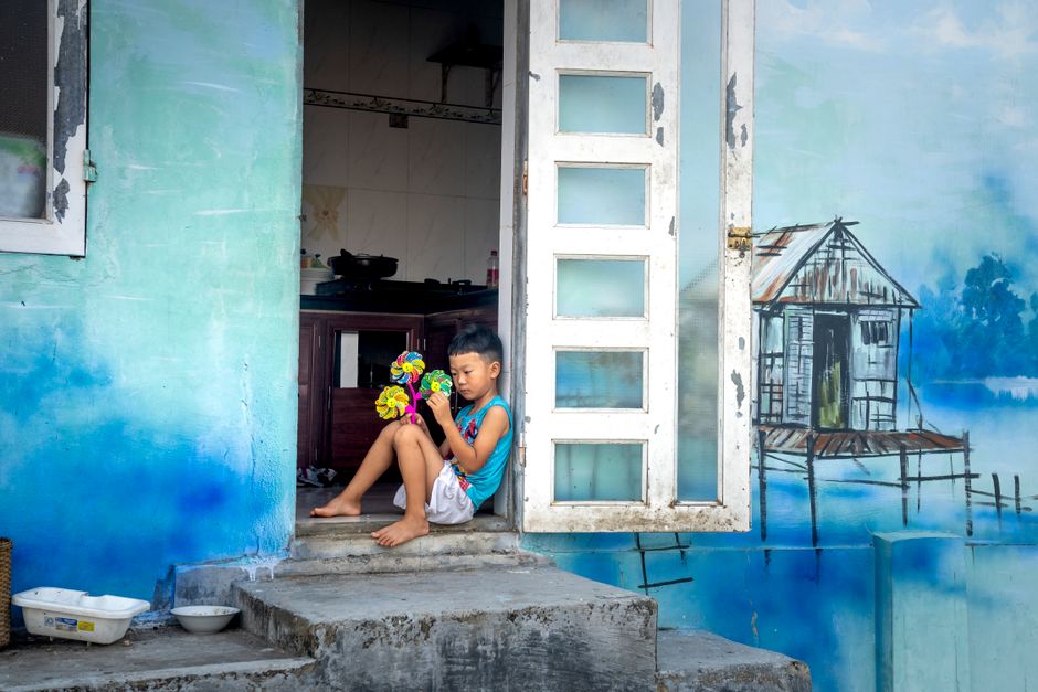 Side view of Asian boy with toy sitting on doorstep of old house near blue graffiti on wall